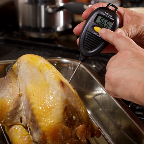 A photo of a person checking food temperature with the RNIB talking food thermometer inserted into a roast chicken and pressing a yellow button to make it speak.