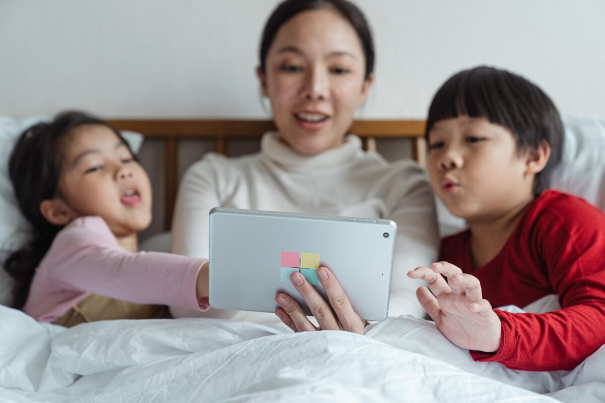 happy ethnic mother and children choosing content on tablet in bed