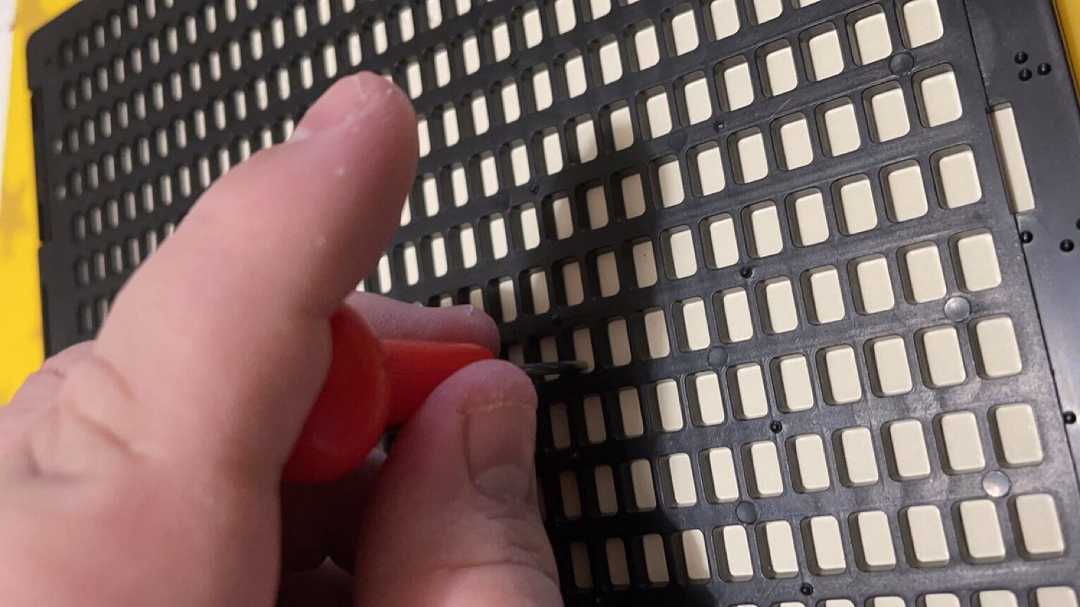 Photo of a hand holding a Braille stylus and pressing into paper held in a Braille frame.