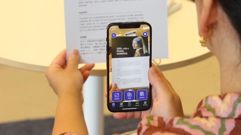 A phone held over a page of text with Envision App reading the text to users with sight loss