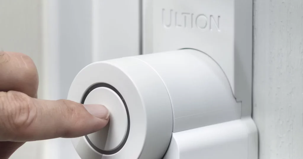 Photo of athe Ultion Nuki Smart Lock, with a finger about to press a finger on the button to instigate the lock.