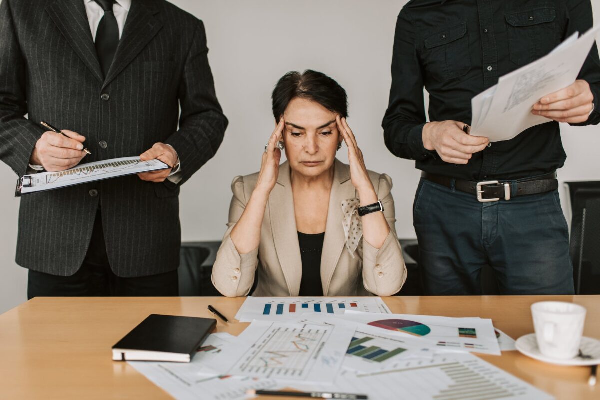 stressed elderly woman holding her head looking at documents laid out in front of her.