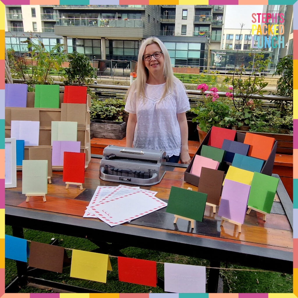 Hayley from Dotty About Braille stood behind a market stall that has braille greetings cards, letters from Father Christmas and a Perkins Brailler displayed.