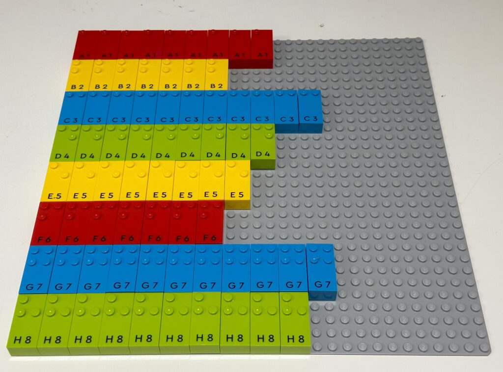 Lego Braille Bricks on a grey Lego base play. From the top left down to bottom left are bricks for a to h. Across are additional bricks of each letter.